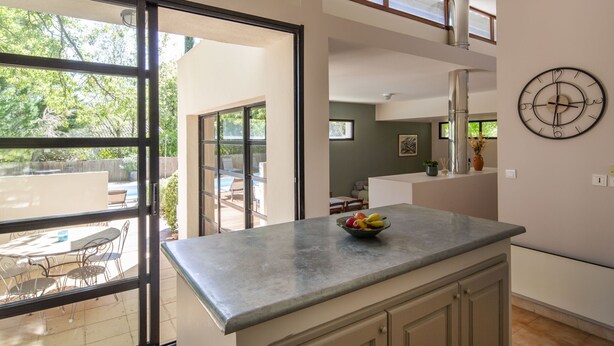Een moderne keuken met een groot eiland, een eethoek met terraszitplaatsen en uitzicht op de natuur.