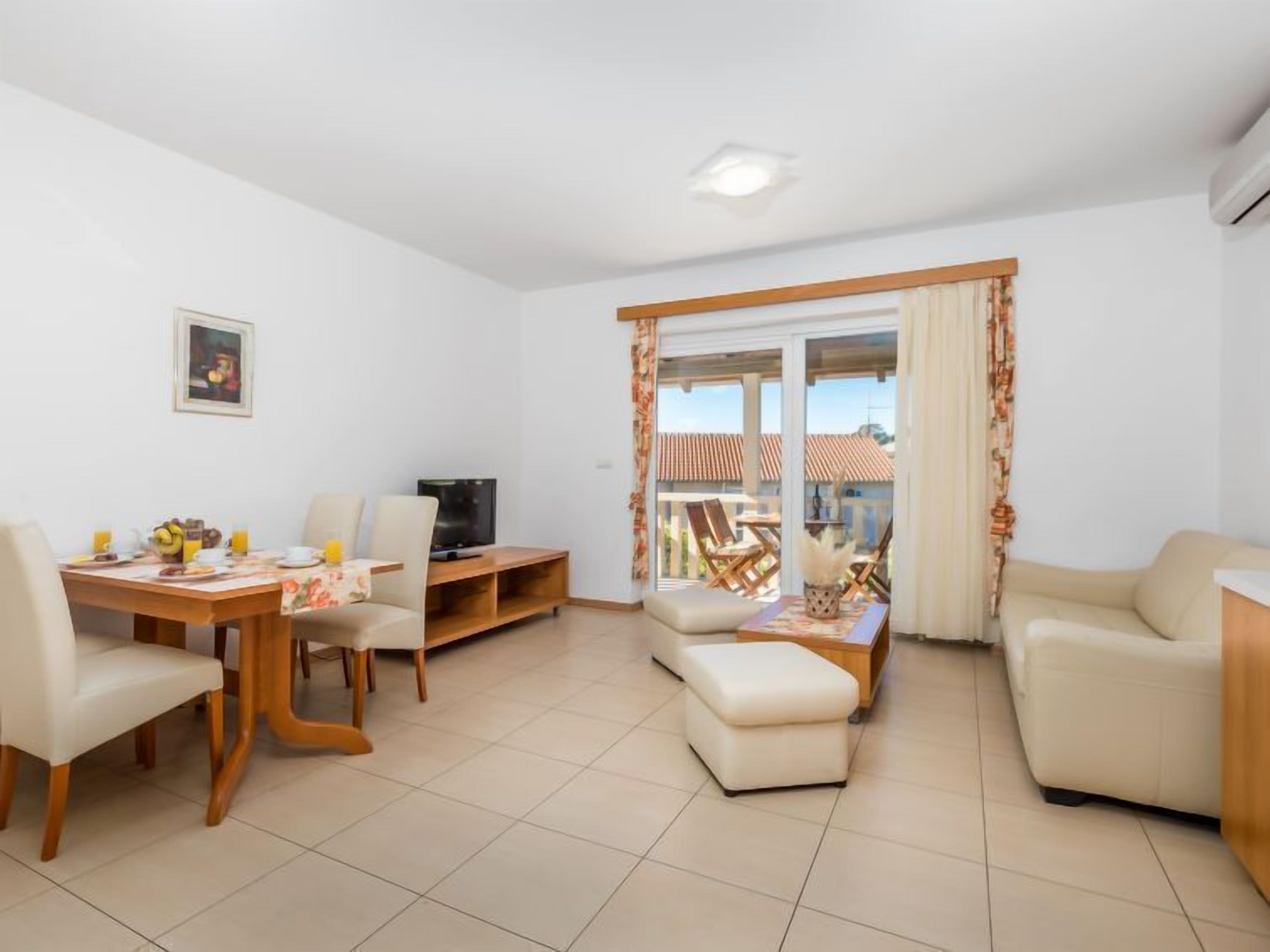 A living room with a dining area, a TV, and a balcony with outdoor furniture.