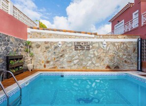 A swimming pool with a stone wall and a wooden deck.