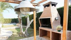 An outdoor brick barbecue area with a stone-tiled patio, a hanging light fixture, and a potted plant. - Vacation home Dirk by Interhome (L'Ampolla)