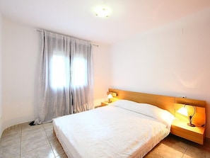 Une chambre d’hôtel avec un lit, des tables de chevet, une lampe et une fenêtre avec des rideaux.