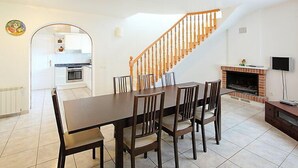 A dining area with a wooden table and chairs, a kitchen in the background, a staircase, and a fireplace with a TV. - Vacation home Dirk by Interhome (L'Ampolla)