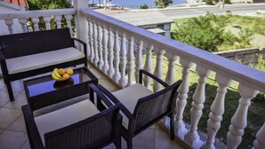 A balcony with a view of the sea, a table with chairs, and a bowl of fruit.
