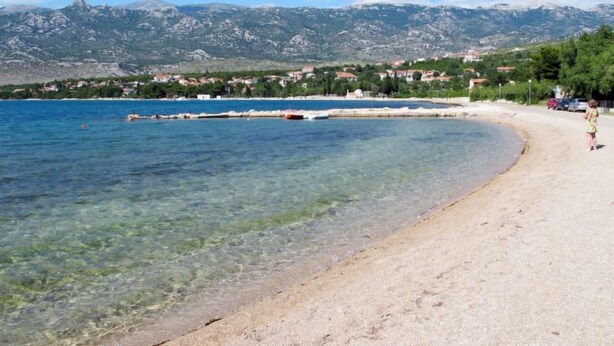 A beach with clear water, a sandy shore, and a mountainous backdrop.