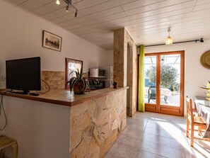 A kitchen with a stone counter, a television, and a view of the outdoors through a glass door.