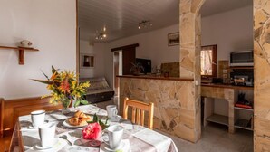 Un'area pranzo con una parete in pietra, un tavolo apparecchiato con croissant, tazze di caffè e un vaso di fiori.