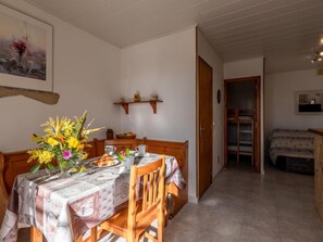 A dining area with a table set for two, a vase of flowers, and a painting on the wall.