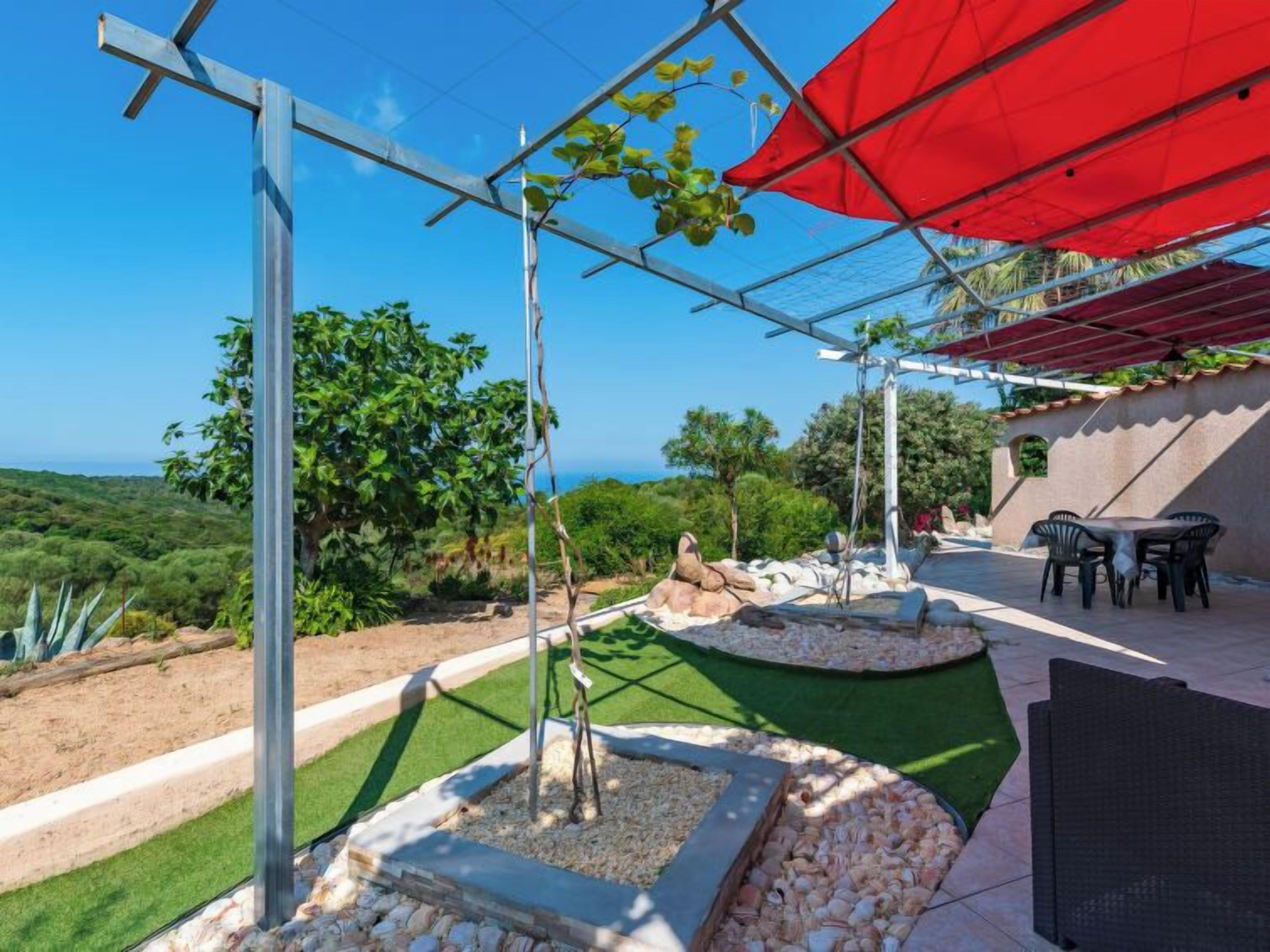 A patio area with a table and chairs, a red umbrella, and a view of the ocean.