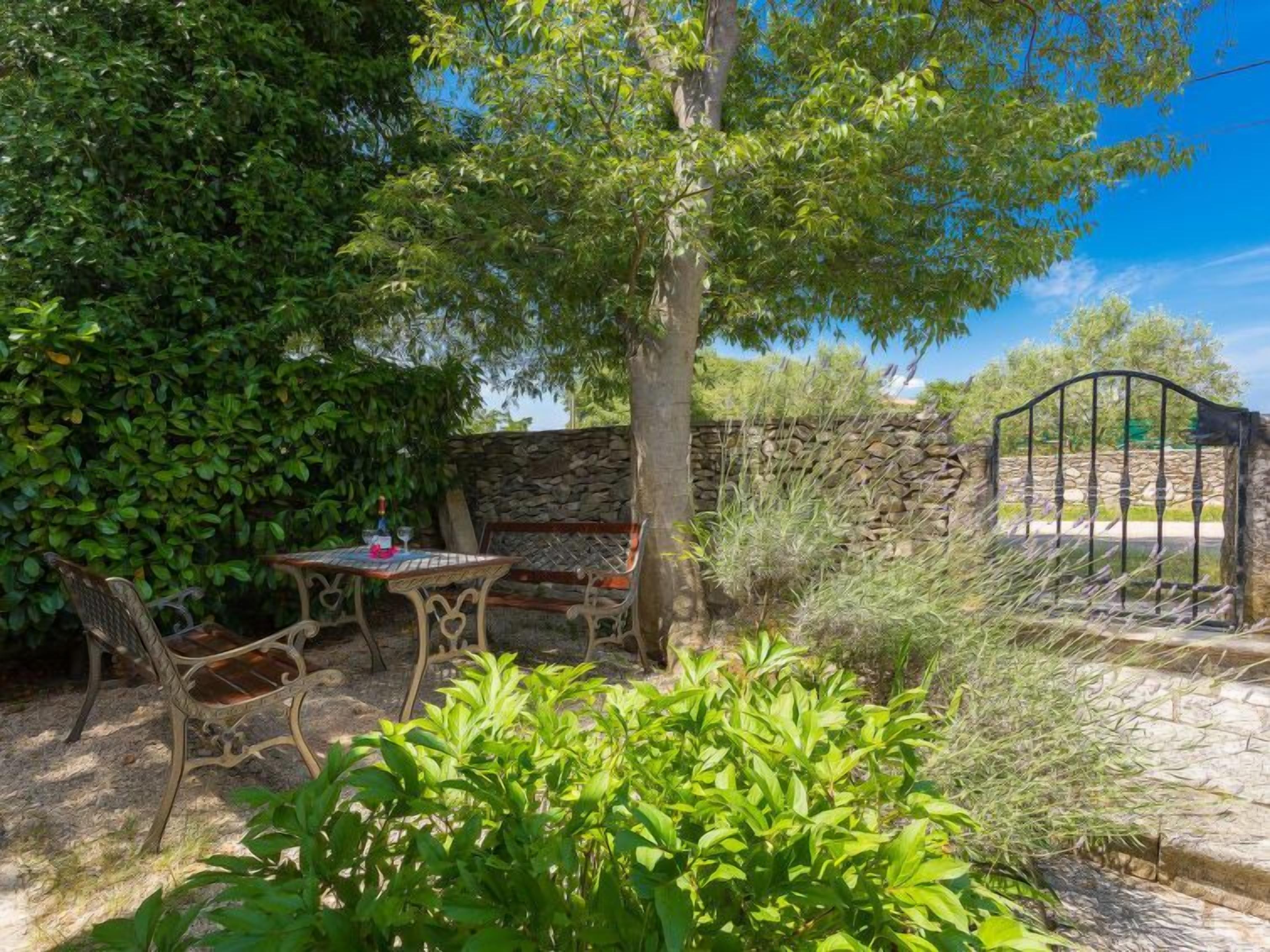 An outdoor patio with a stone wall, a wrought iron gate, and a table with chairs.