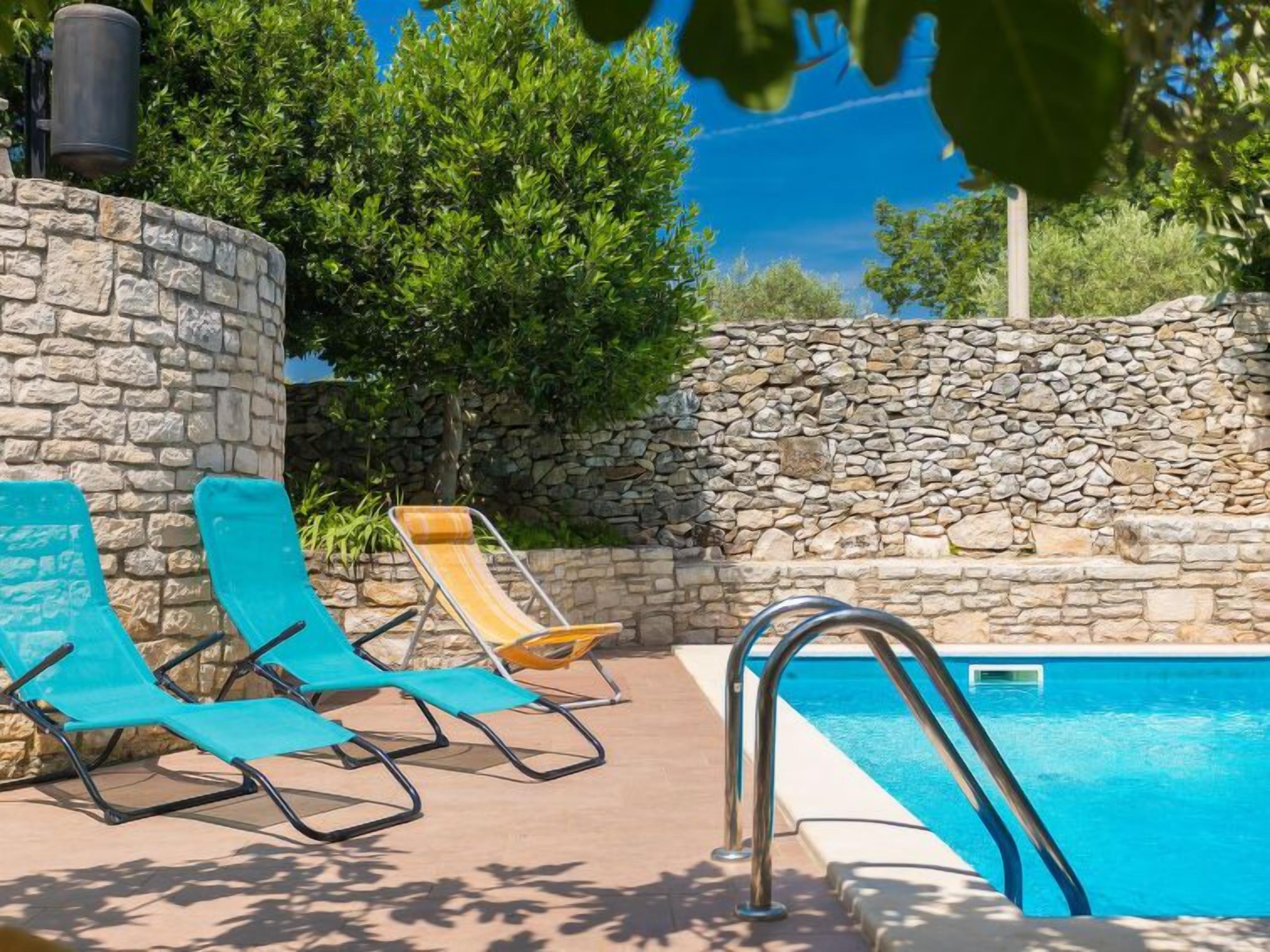 Ein Poolbereich mit Steinwänden, zwei Liegestühlen und einem Pool.