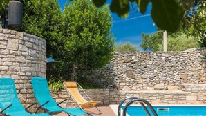 Zona de piscina con muros de piedra, dos sillones reclinables y una pileta.