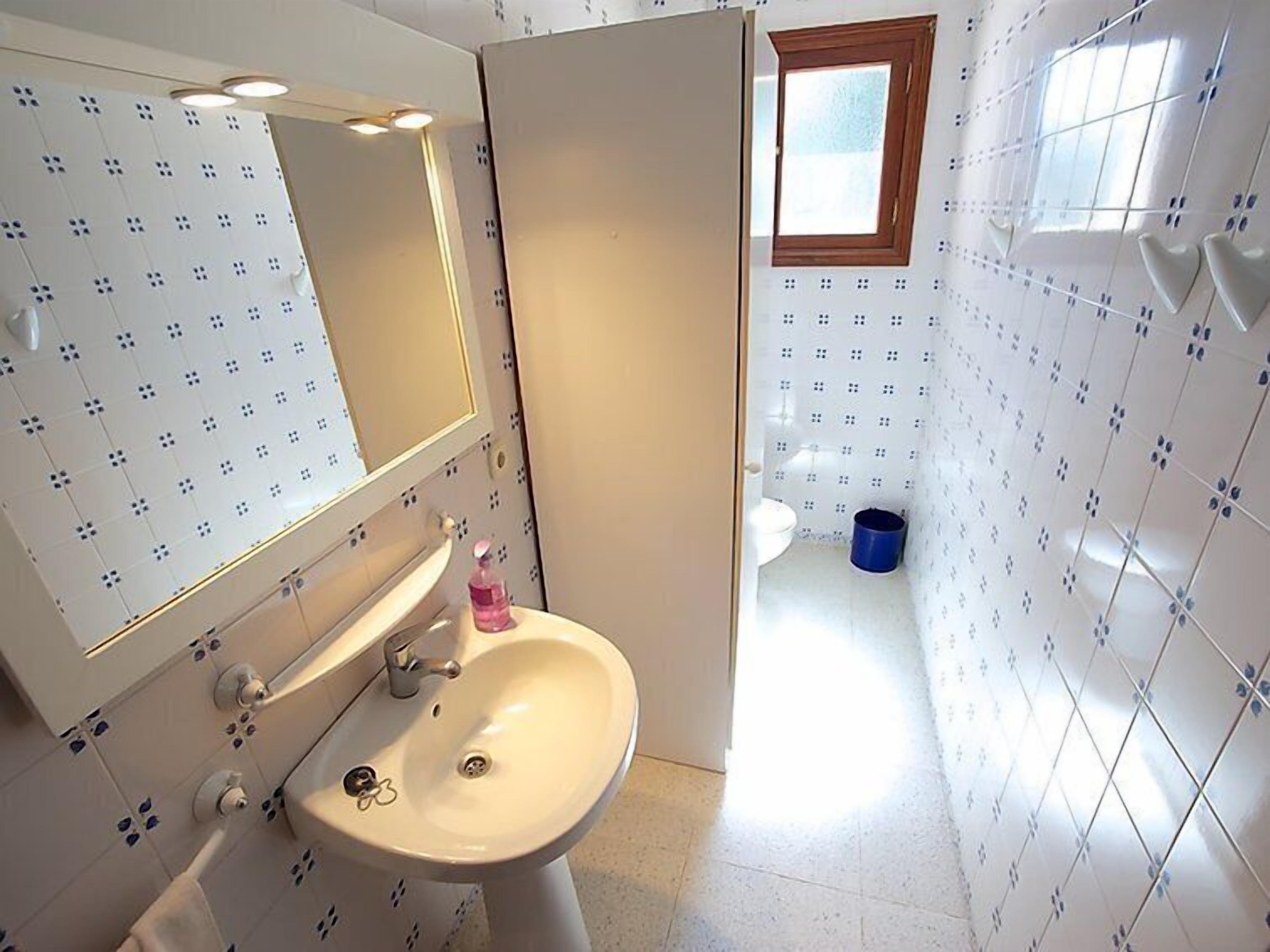A bathroom with a white sink, mirror, and tiled walls.