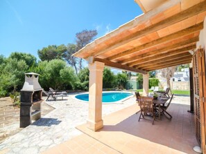 Uma área externa coberta com piscina, móveis de pátio e churrasqueira.