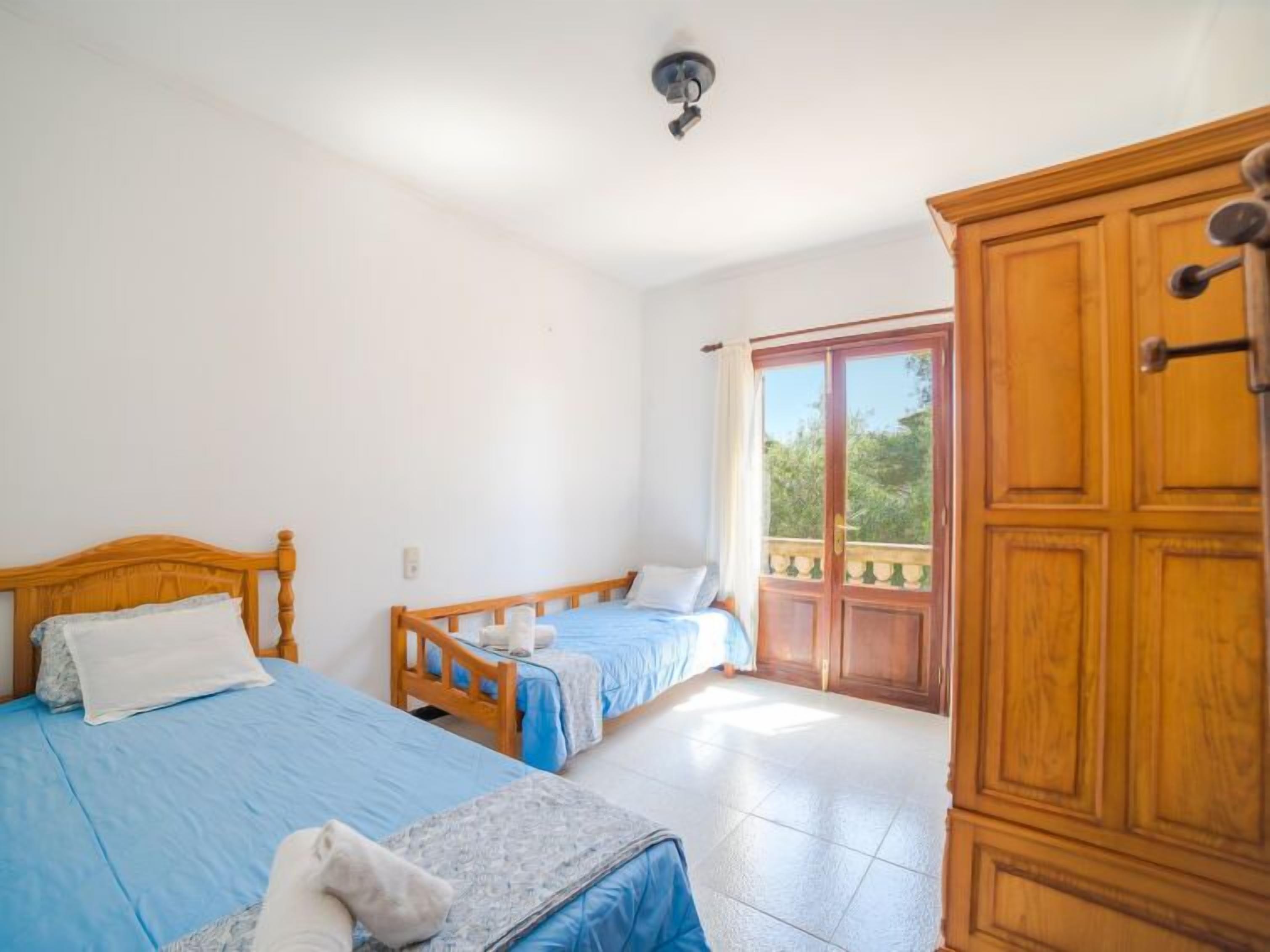 A bedroom with two beds, a wooden wardrobe, and a balcony with a view.
