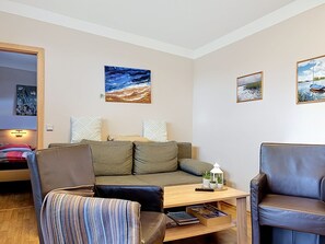A modern living room with a sofa, two armchairs, a wooden coffee table, and wall art.