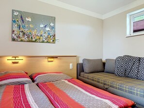 Une chambre d’hôtel avec deux lits, un canapé, un tableau au mur et une fenêtre avec des stores.