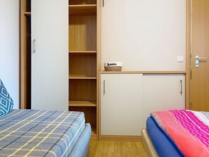 Un dormitorio con dos camas, un armario y una estantería con una cesta.