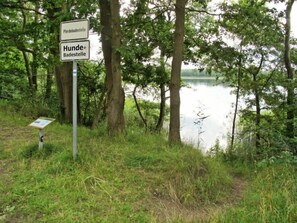 Wegwijzer met de aanduiding 'Pferdebadestelle' en 'Hondenzwemplaats', omgeven door bomen en een meer.