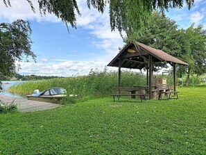 Un belvédère avec une table de pique-nique, un bateau amarré à un quai en bois et une zone herbeuse avec des arbres.