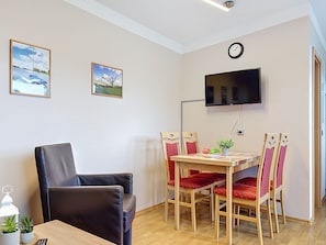 Una habitación con una mesa de comedor de madera, sillas rojas, una butaca de cuero negro, un televisor de pantalla plana montado en la pared y dos cuadros enmarcados.
