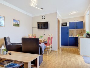 A compact living space with a dining area, a kitchenette, and a television mounted on the wall.