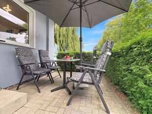 Un patio al aire libre con una mesa, dos sillas, una sombrilla y vista a un sauce llorón.