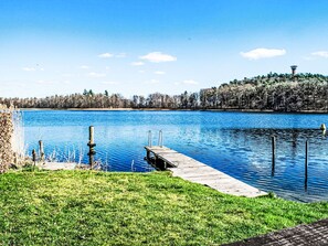 Een meer met een houten steiger die in het water uitloopt, omringd door grasvelden en bomen.