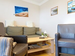 Una sala de estar con sofá, dos sillones, una mesa de centro y una estantería.