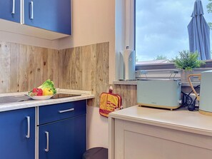 Una cocina moderna con armarios azules, un protector contra salpicaduras de madera y una ventana con vistas a un jardín.