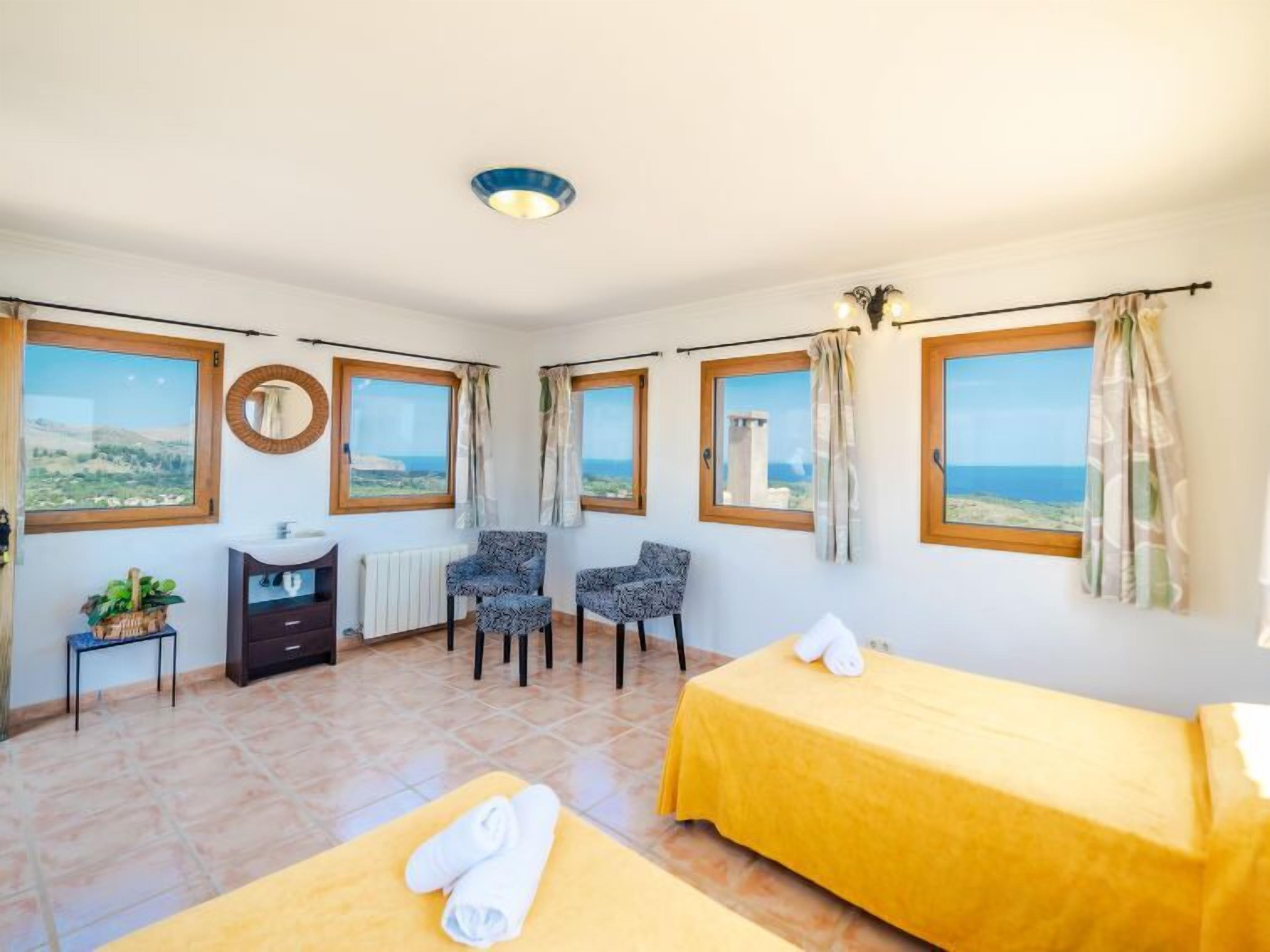 A hotel room with two beds, a small desk, a mirror, and a view of the sea.