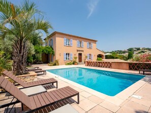 Ein zweistöckiges Haus mit Swimmingpool, umgeben von Palmen und blauem Himmel.