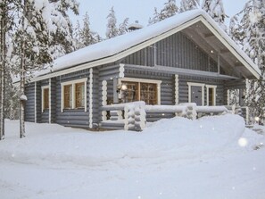 Une cabane en rondins avec un toit enneigé, une véranda en bois et une fenêtre donnant sur le paysage enneigé environnant.