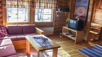 Ein gemütliches Blockhauss-Interieur mit einer Couch, einem Fernseher und einem kleinen Tisch.