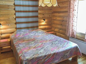 A room with a bed, wooden walls, a window with curtains, and two wall-mounted lights.