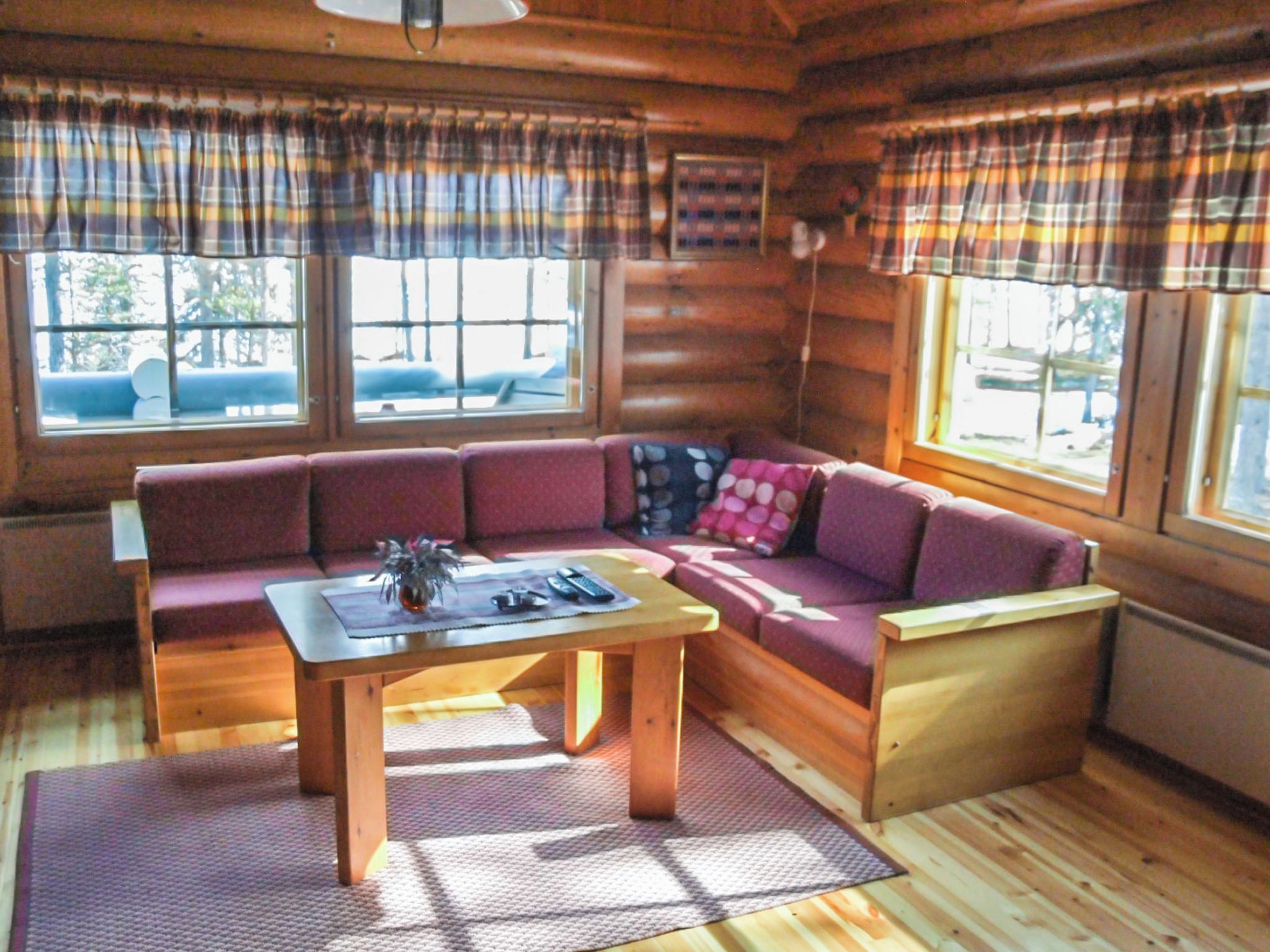 A log cabin interior with a wooden sofa, a small table, and plaid curtains.
