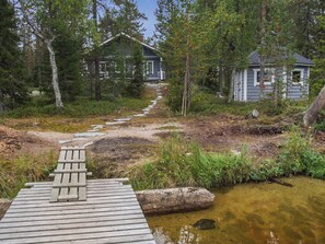 A wooden deck leading to a rustic cabin surrounded by trees and a small stream. - Kujalan lomat 2 by Interhome (Kuusamo)