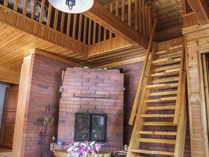 Un intérieur en bois avec une cheminée en briques, un escalier en bois et un luminaire suspendu.