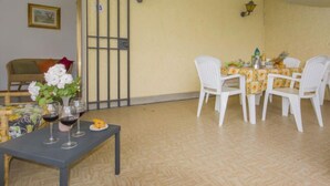 A dining area with a table set for four, white chairs, and a small table with wine glasses and a plate of food. - Magnolia by Interhome (Montaione)