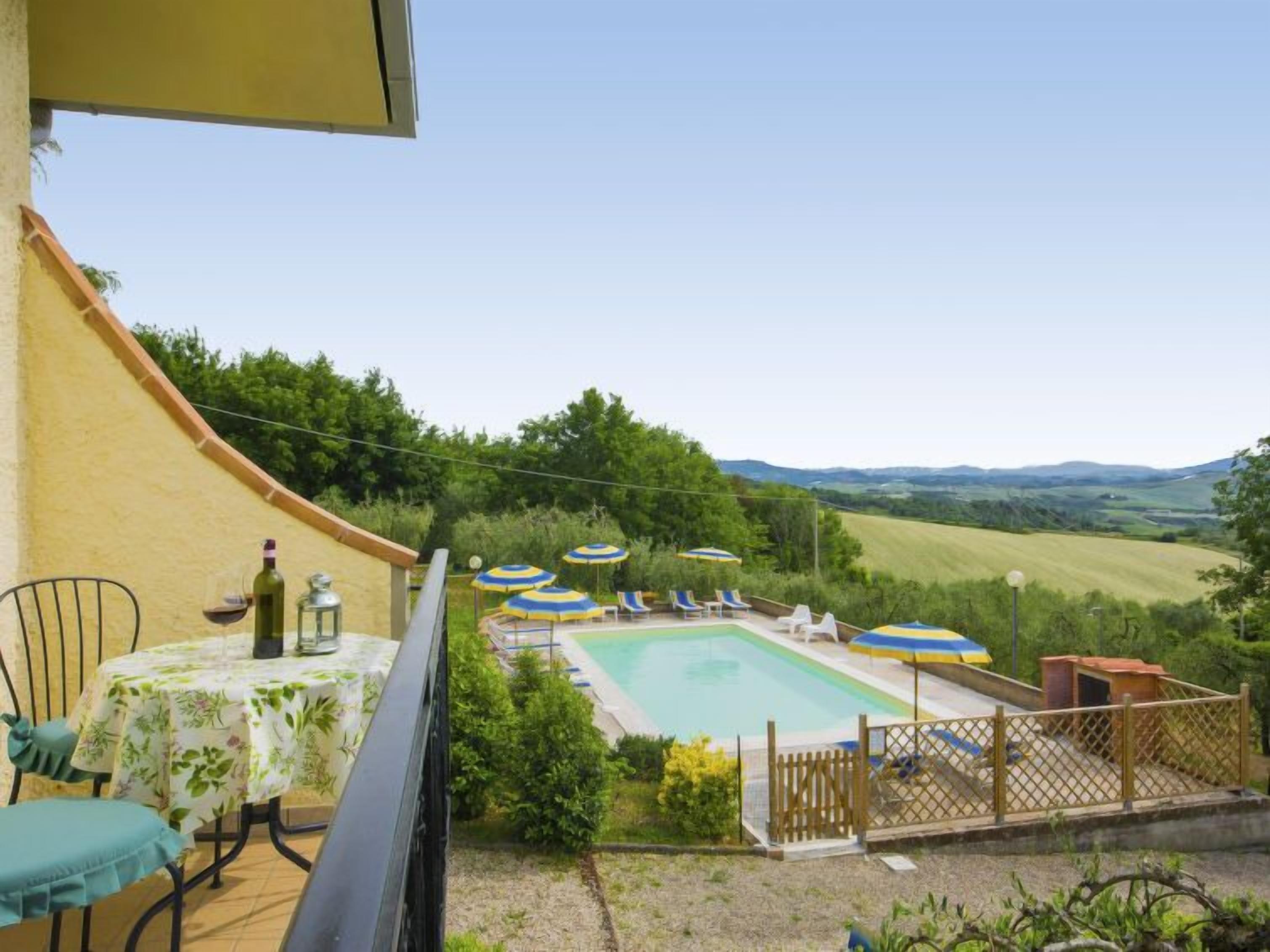 A pool area with lounge chairs and umbrellas, a table with a bottle and glass, and a view of the countryside.