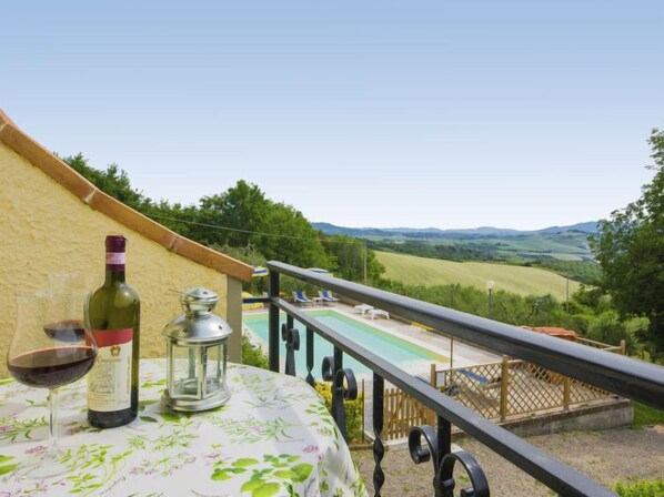 A balcony with a table set for two, a bottle of wine, and a lantern. A pool is visible in the background.