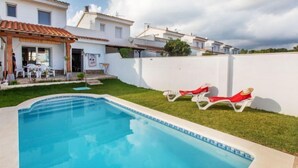 Una piscina con sillones de descanso, un área de patio y un edificio blanco con tejado de tejas.
