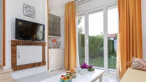 Una sala moderna con televisor de pantalla plana, una mesa de comedor con comida, un sofá y un ventanal corredizo al exterior.