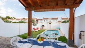 Un patio al aire libre con una mesa lista para comer, una piscina al fondo y vistas a casas vecinas.