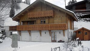 Una cabaña de madera con balcón, garaje y una pequeña construcción adosada.