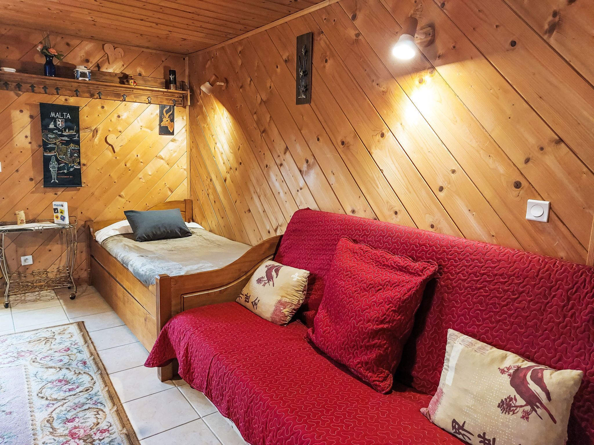 Een gezellige kamer met een houten plafond, een bed met een rode deken, een houten bank en een kleine tafel met een vaas.