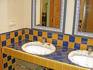 Een badkamer met twee wasbakken, tegels in geel en blauw, en een spiegel met een decoratieve rand.