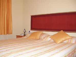 Een hotelkamer met een groot bed, twee kussens, een nachtkastje met een lamp en een rode hoofdbord.