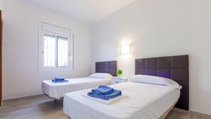 Una habitación de hotel con dos camas, una ventana, una mesita de noche con lámpara y una planta pequeña.
