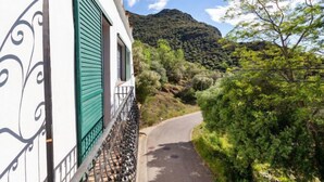 Un bâtiment doté d’un balcon, une route qui tourne vers la droite et un paysage montagneux en arrière-plan.