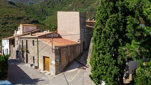 Une rue étroite bordée d’immeubles en pierre, avec un bar et une vue sur une colline où se dresse une structure ressemblant à un château au loin.